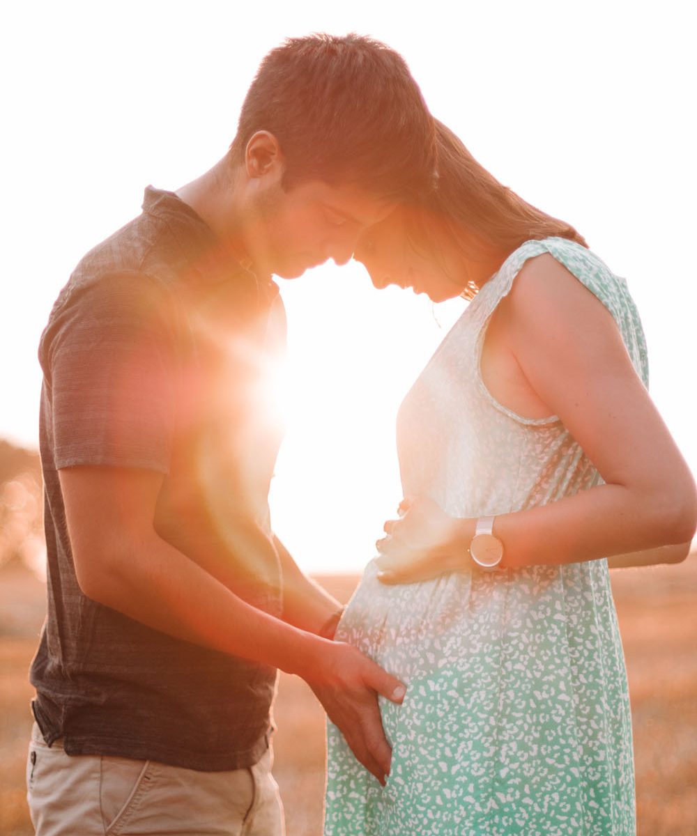 Photo de grossesse un couple regarde le ventre de la femme enceinte dans le soleil couchant dans un champ de blé en Belgique Nivelles