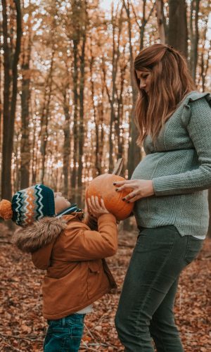 Photo grossesse maman et enfant qui tiennent un potiron en automne dans les bois