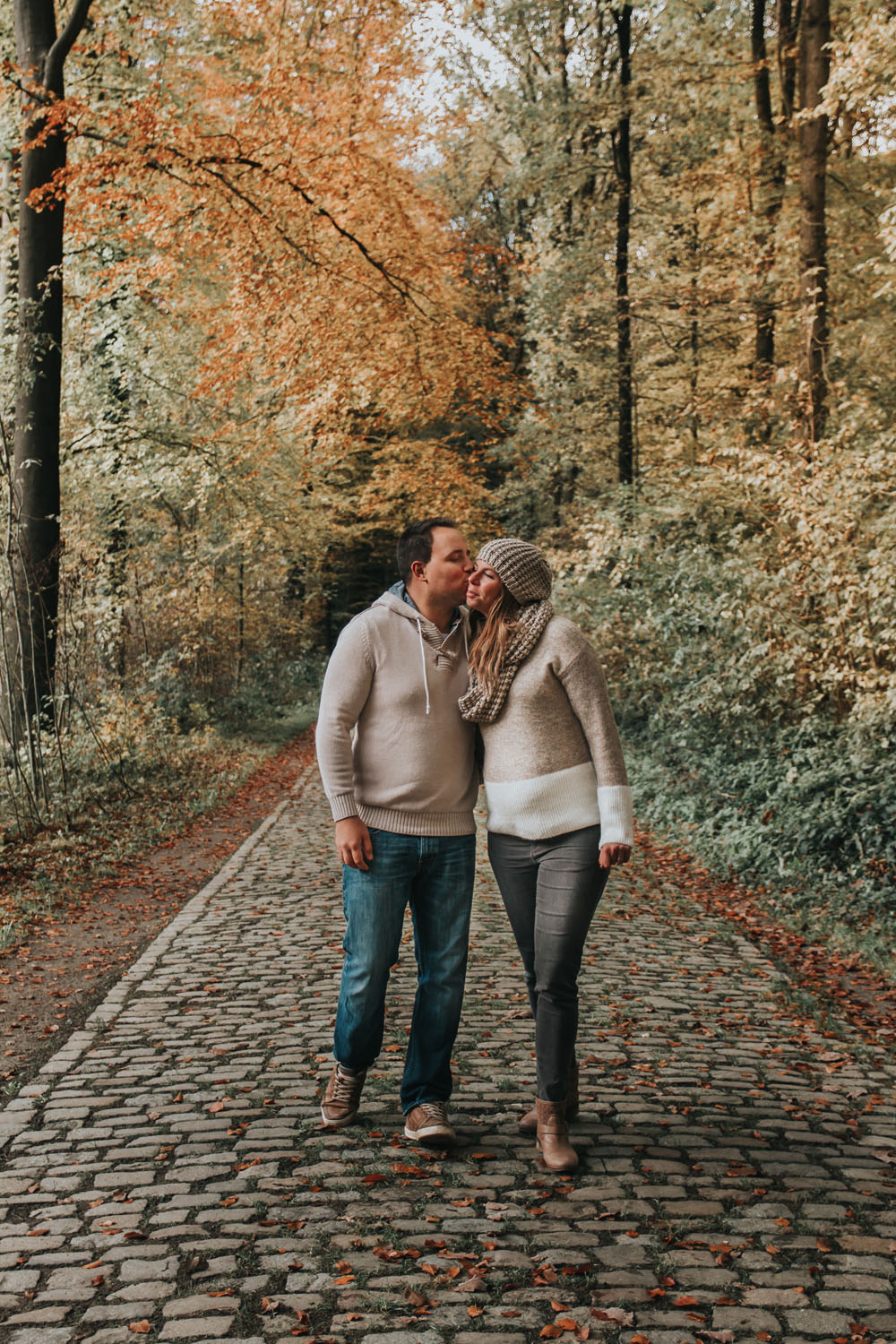 Couple avec femme enceinte en automne qui marchent dans les bois en s'embrassant en Belgique brabant wallon
