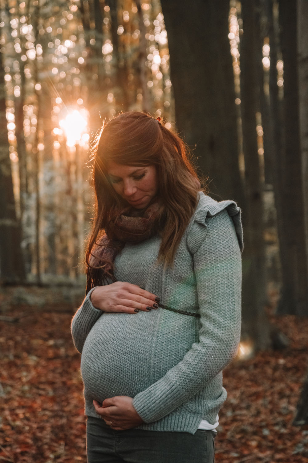 Séance photo grossesse maman qui touche son ventre au coucher de soleil en automne dans les bois